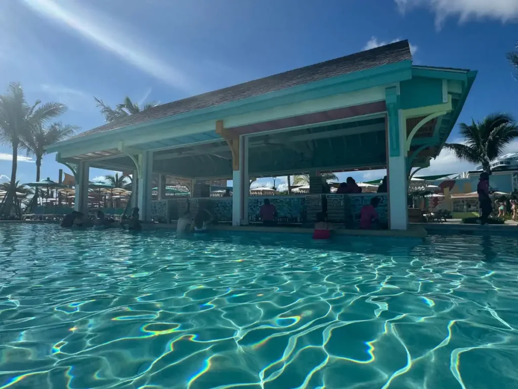 An outdoor pool bar structure overlooking clear blue water and sandy shores in Nassau.