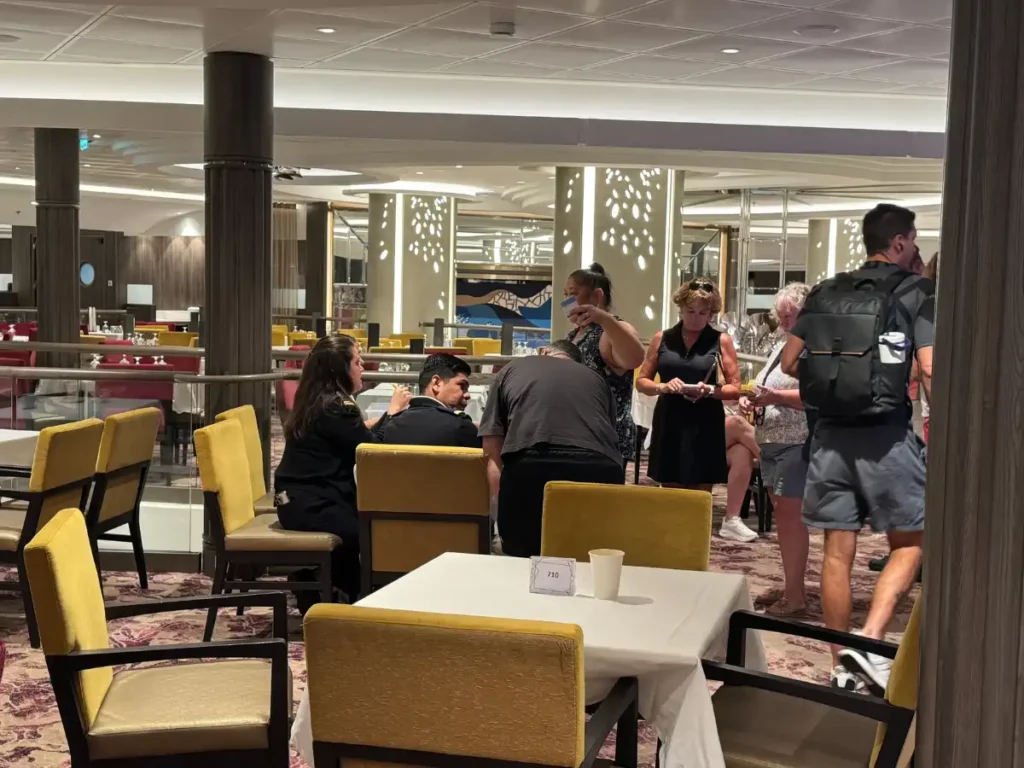 Guests completing back-to-back check-in procedures at tables inside the Main Dining Room on Utopia of the Seas.