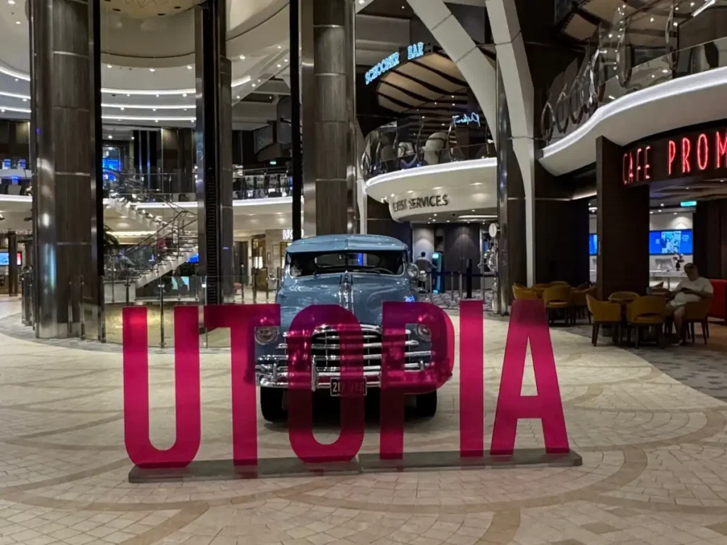 The quiet Royal Promenade on Utopia of the Seas featuring a vintage blue car and overlaid text reading UTOPIA.