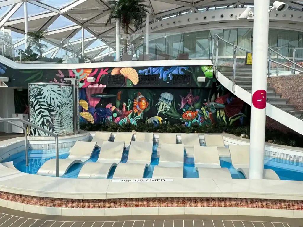 An empty Solarium lounging area with lounge chairs and vibrant ocean-themed wall art on Royal Caribbean's Utopia of the Seas.